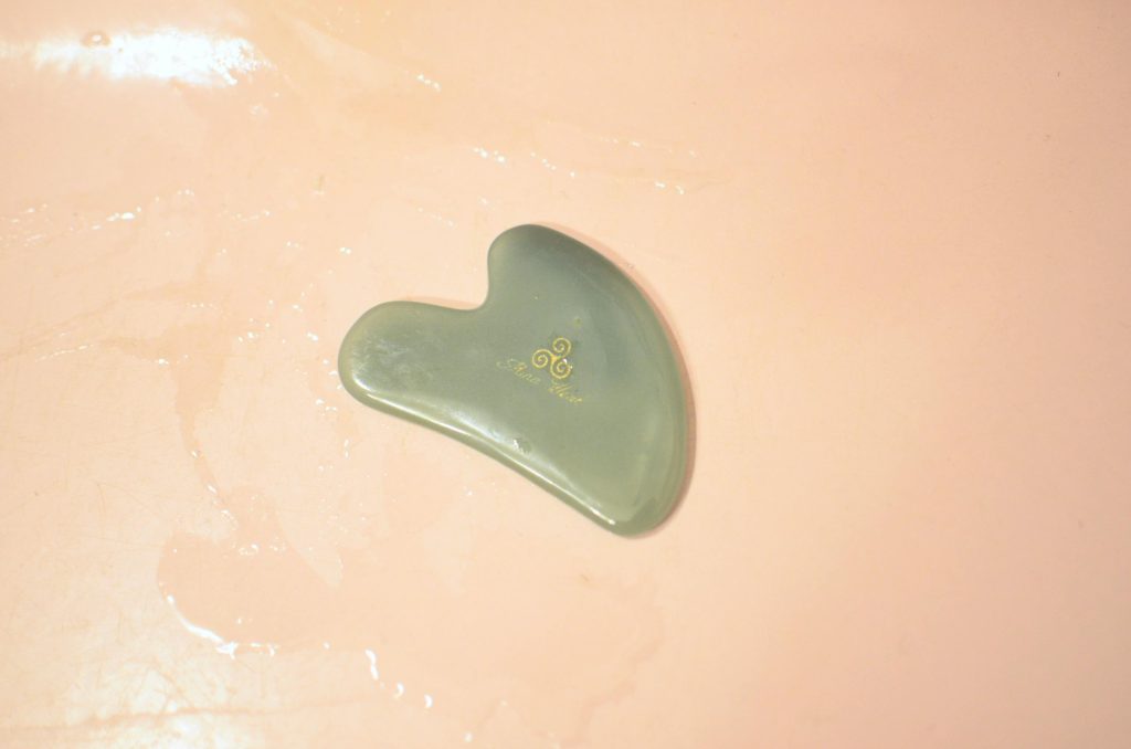 Close-up of a jade gua sha tool on a pink wet surface, ideal for skincare routines.
